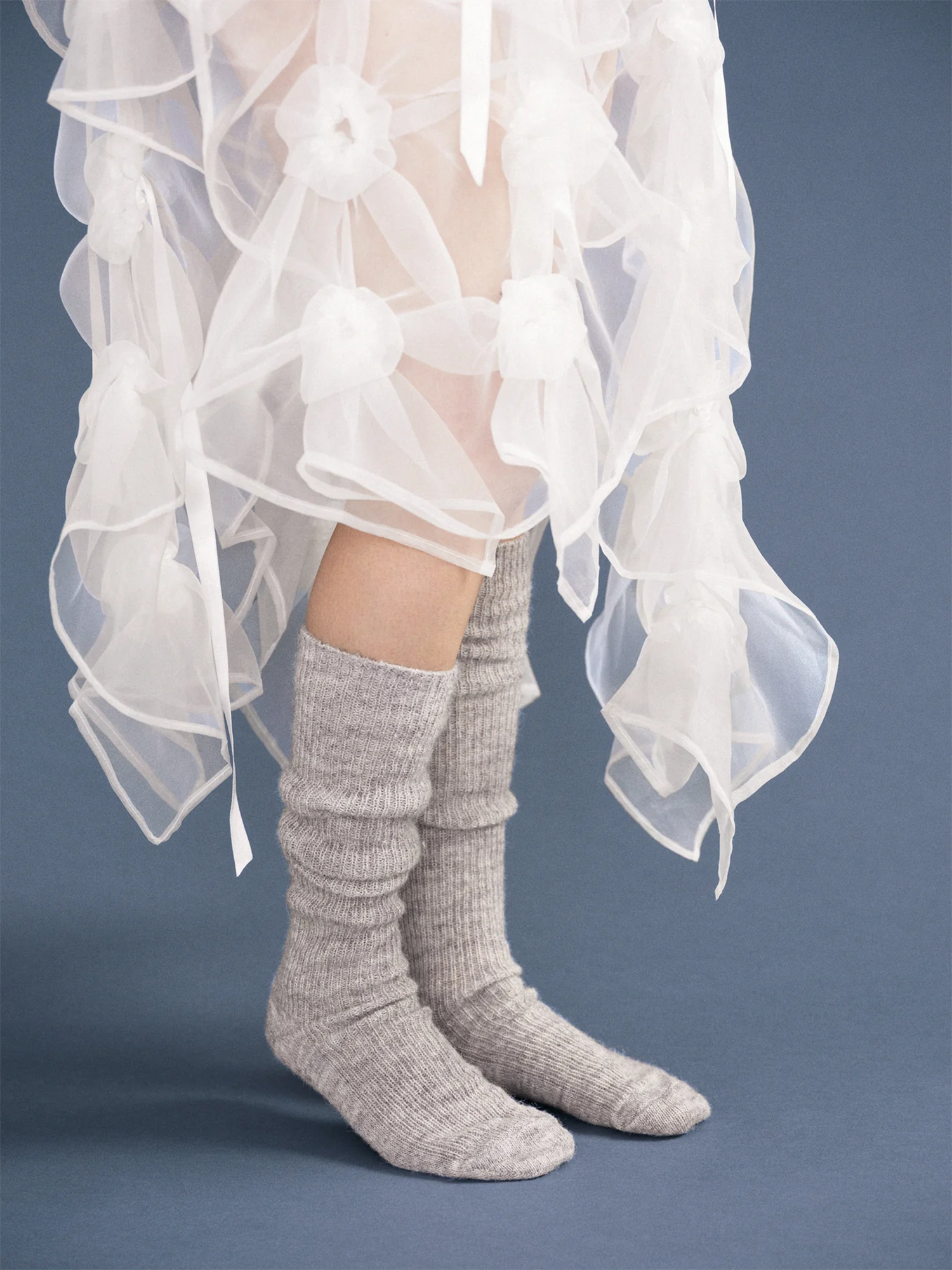 Gray knee-high socks worn with a white sheer fabric skirt on a blue background