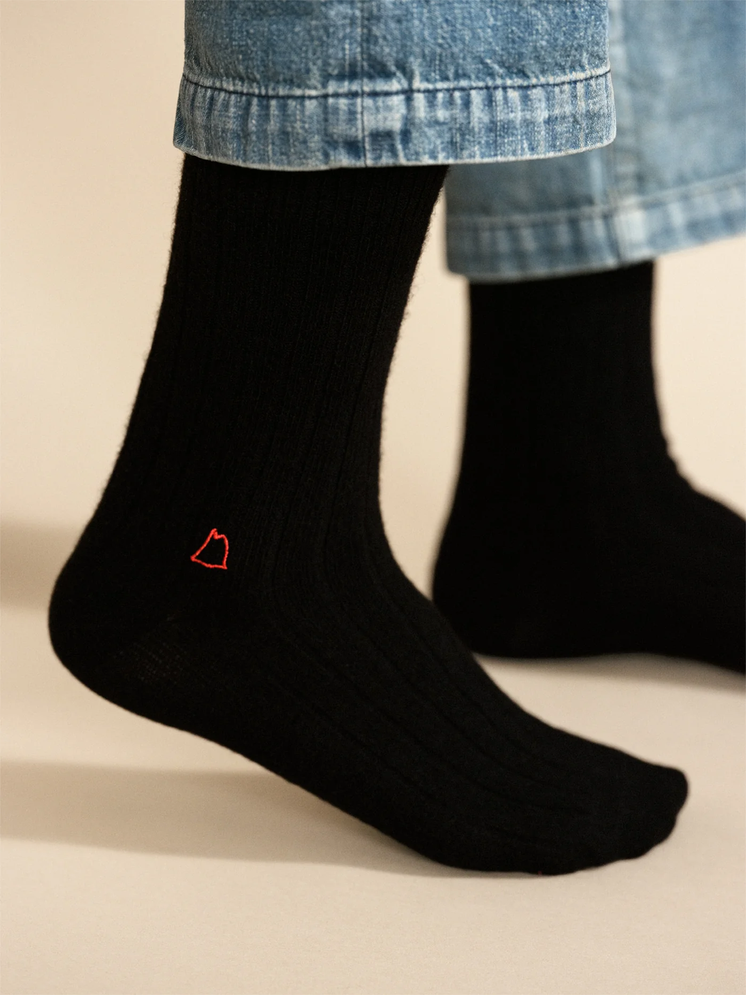 Black socks with a red logo worn with blue jeans on a beige background