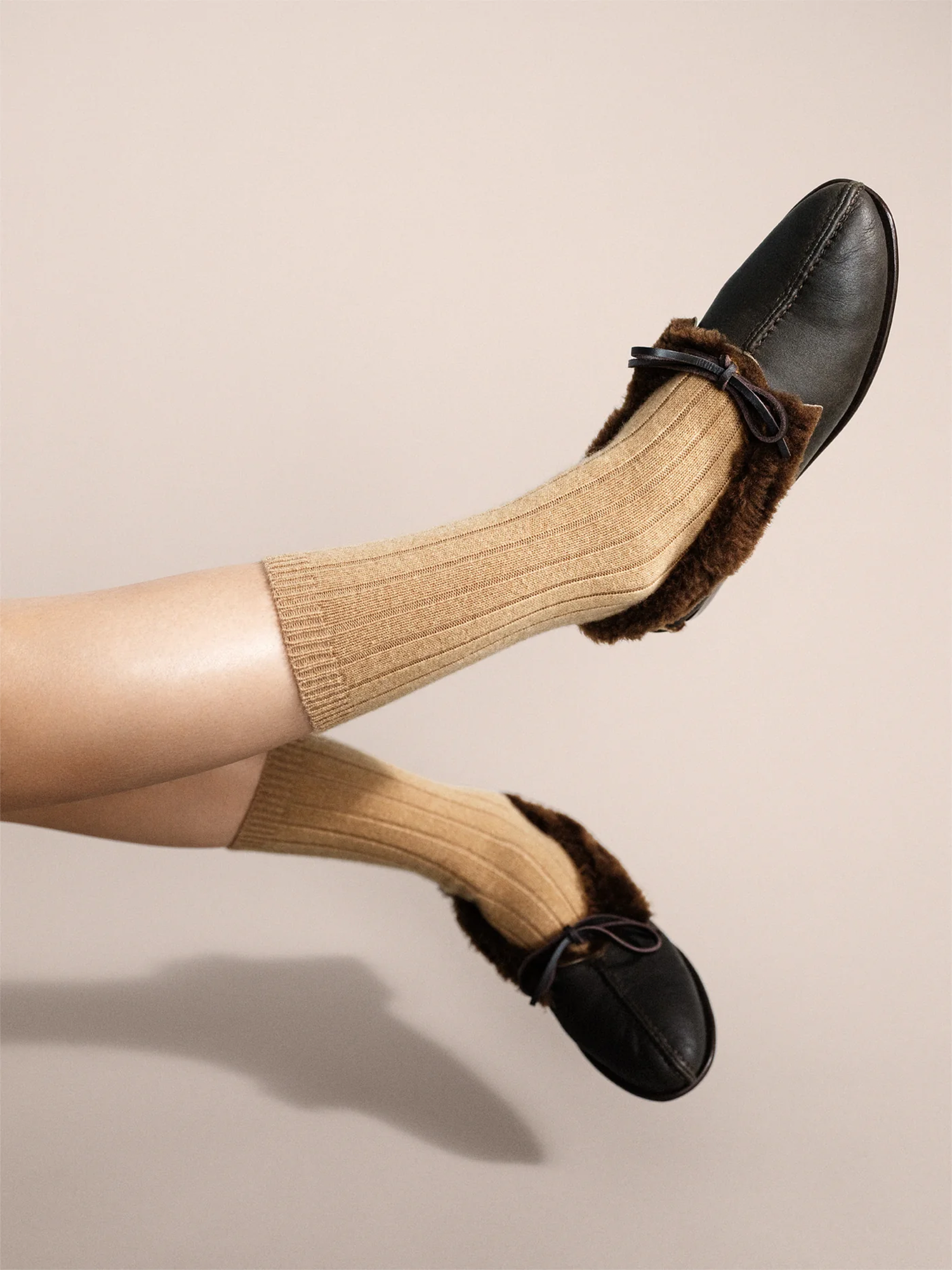 Black loafers with brown fur trim worn with beige knee-high socks on a beige background