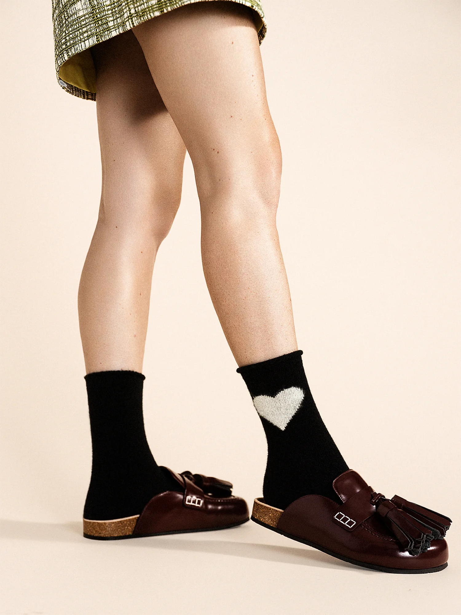 Person wearing black socks with a heart design and brown shoes on a beige background
