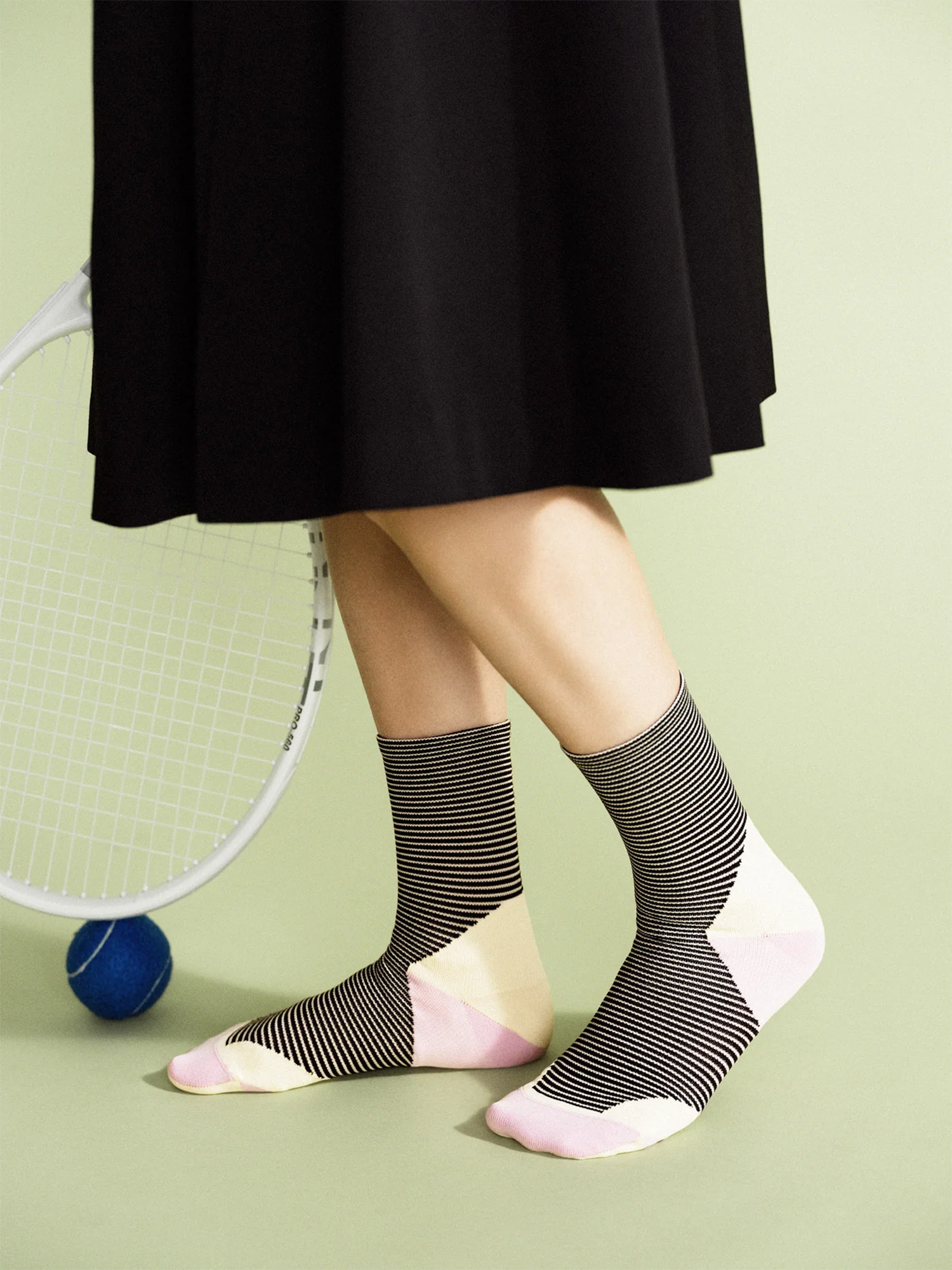 Person wearing striped socks with a tennis racket and ball on a light green background