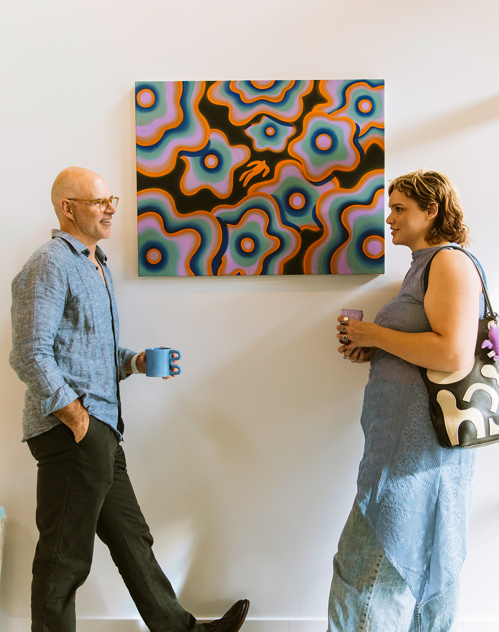 Two people standing in a room with a colorful abstract painting on the wall.