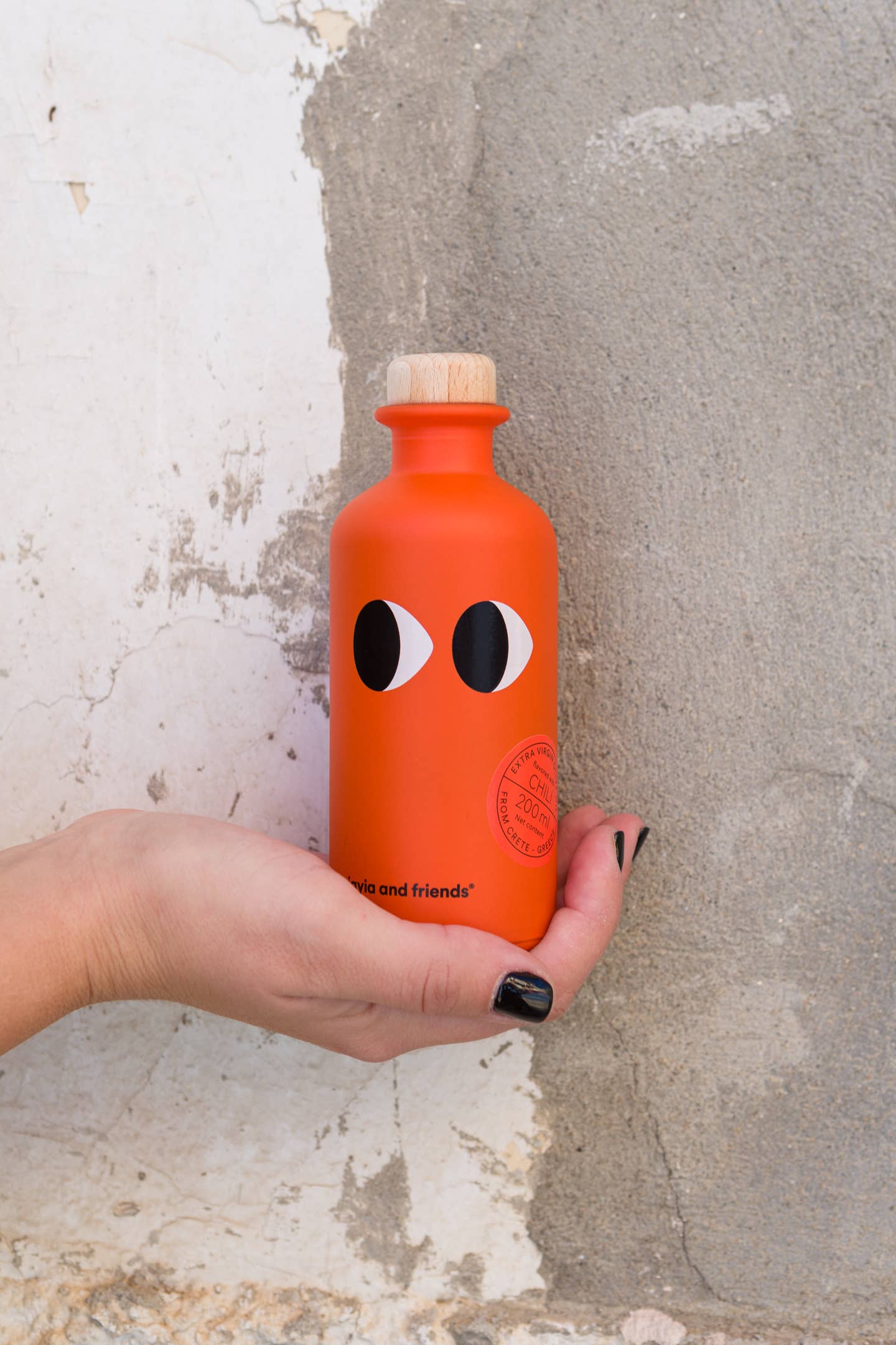 Hand holding an orange bottle with a face design against a textured wall.