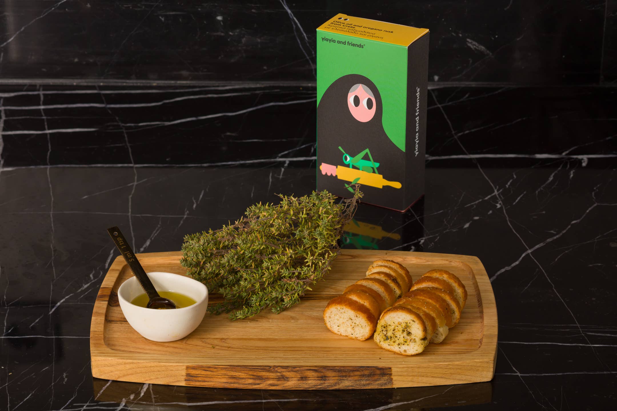 Wooden tray with thyme, a bowl of oil, and sliced bread on a black marble surface.